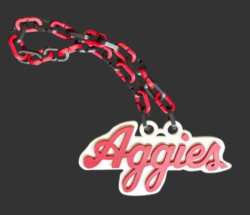 A custom chain necklace featuring red and black interlocking links and a white pendant with the word 'Aggies' in red cursive script, displayed on a dark gray textured background.
