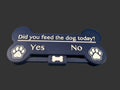 A bone-shaped pet feeder tray in dark navy blue with white text reading 'Did you feed the dog today? Yes No' and paw print icons on both ends, resting on a blue surface.
